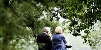 two people sitting on pavement facing on body of water